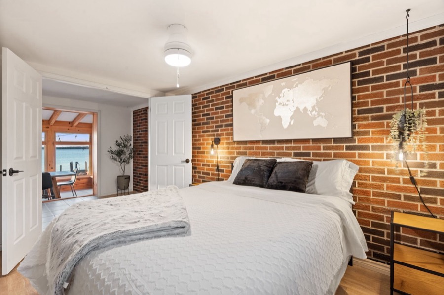 Bedroom with an exposed brick wall and a view through to the sunroom and water