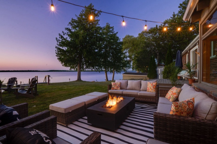 Lounge seating around the fire table under string lights, with the bay at dusk