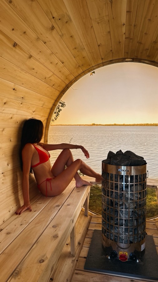 Guest relaxing in the panoramic barrel sauna, looking out over the bay at sunset