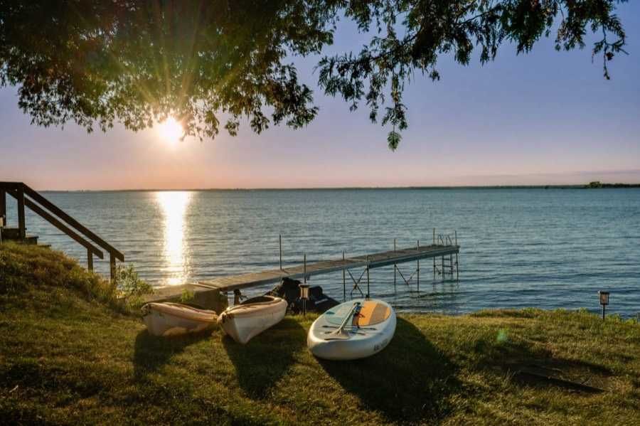 Kayaks and paddleboard on the lawn beside the dock at sunset